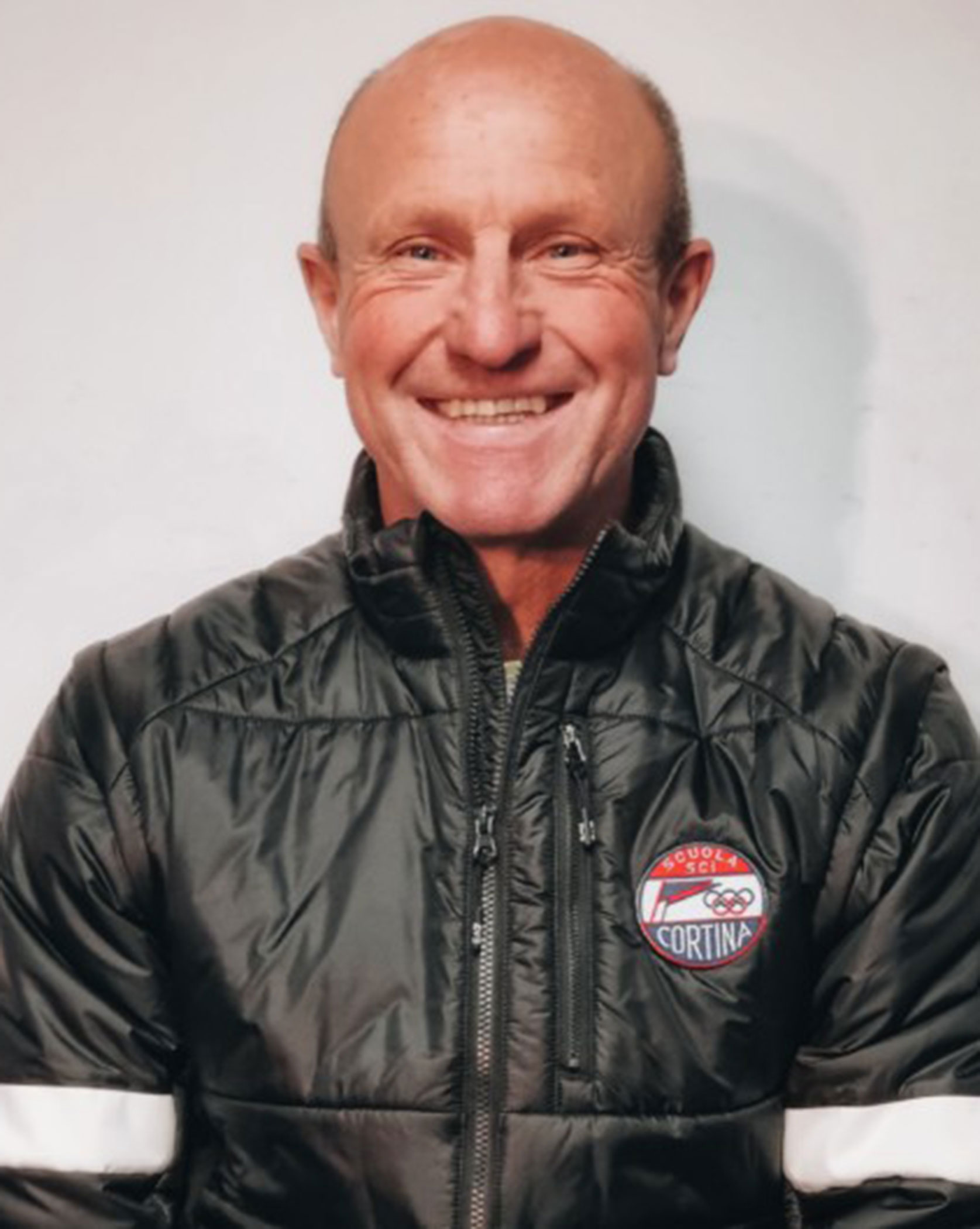 Smiling man in a black Cortina jacket stands against a plain white background. - Scuola Sci Cortina