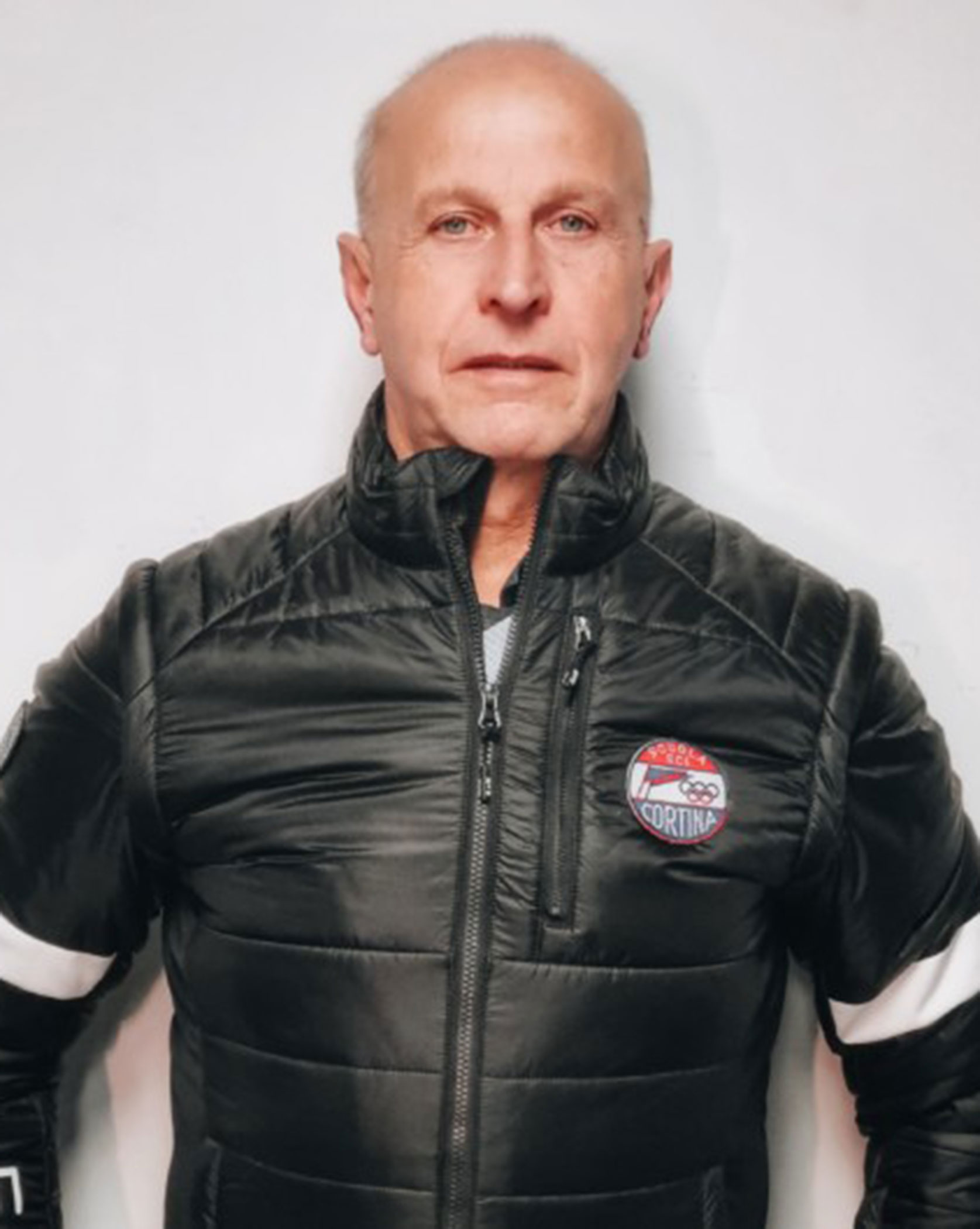 Bald man in a black puffer jacket stands against a plain white background, facing the camera. - Scuola Sci Cortina