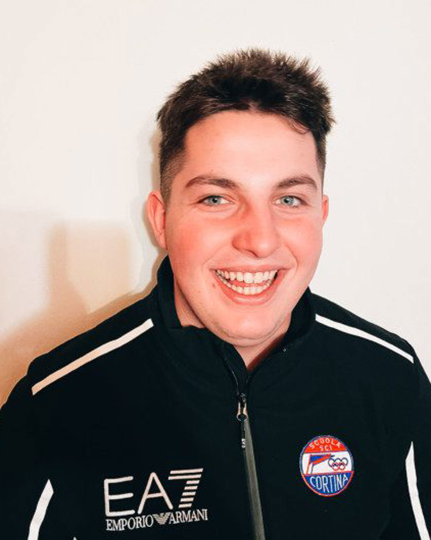 Smiling young man in a black EA7 Emporio Armani jacket with a Scuola Sci Cortina logo on it. - Scuola Sci Cortina