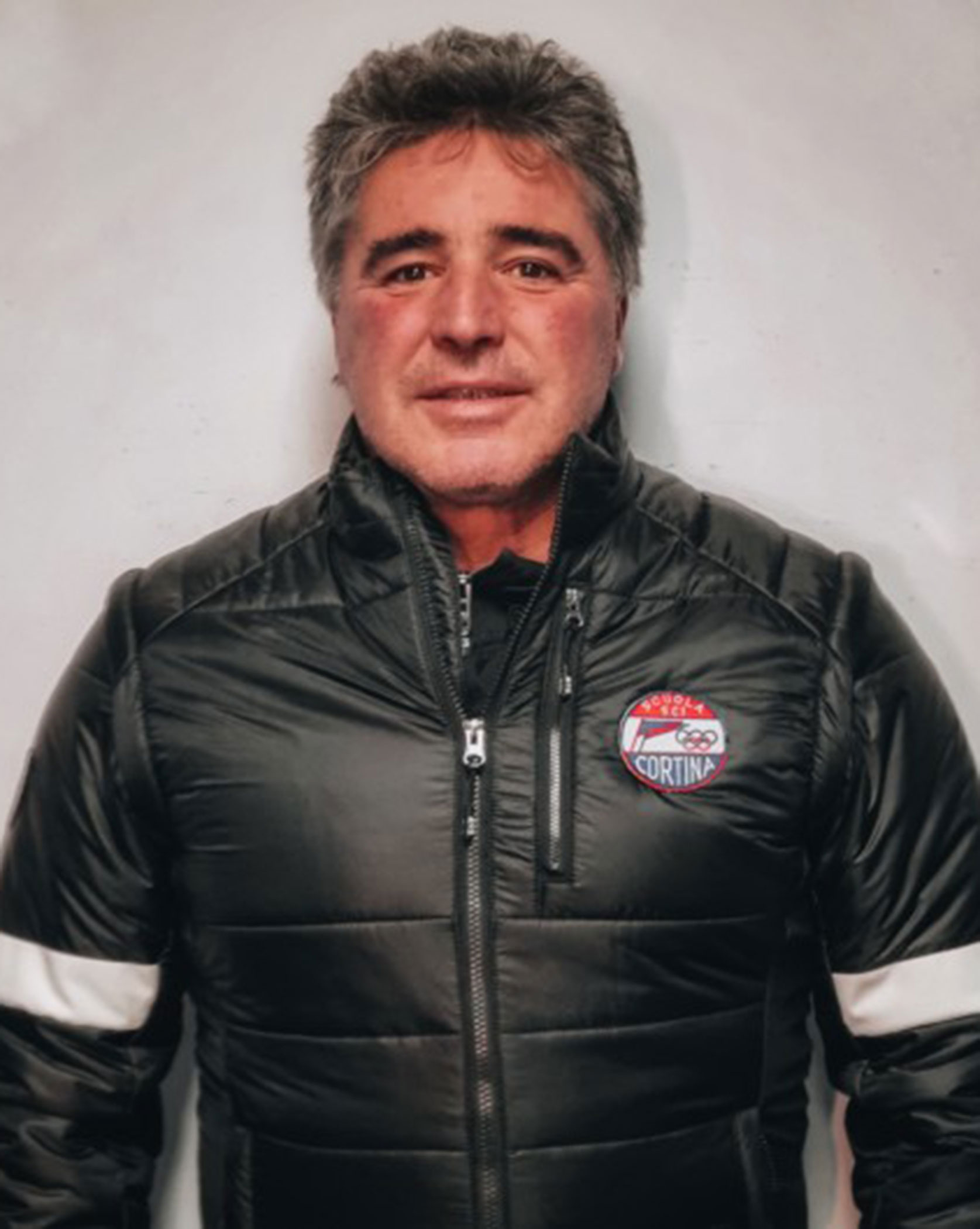 Man in a black puffer jacket with a Cortina patch stands against a plain white background. - Scuola Sci Cortina