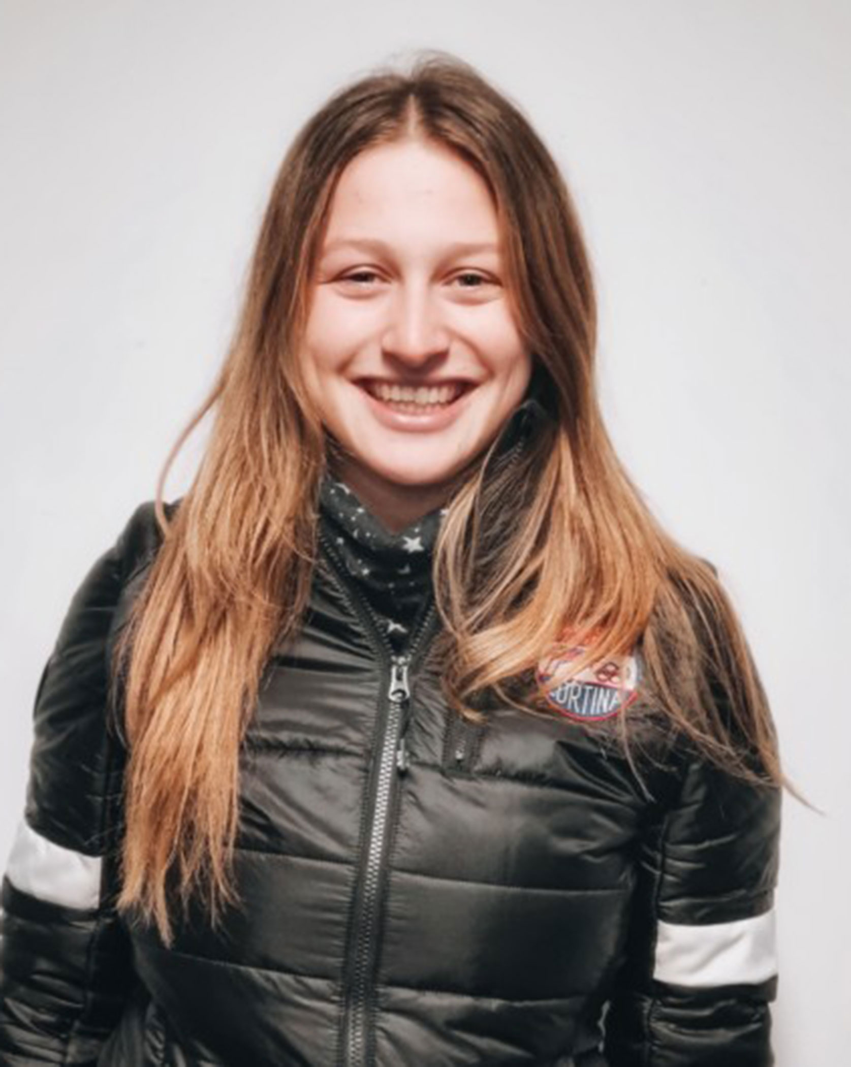 Smiling young woman in a black jacket with long brown hair against a plain white background. - Scuola Sci Cortina