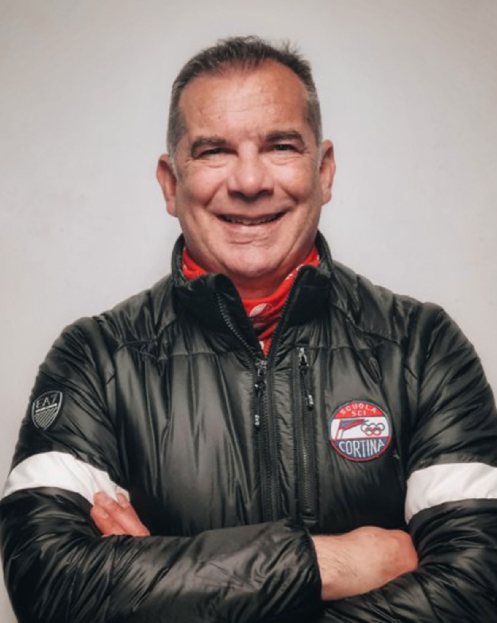 Smiling man in a black jacket with crossed arms, posing against a plain light background. - Scuola Sci Cortina