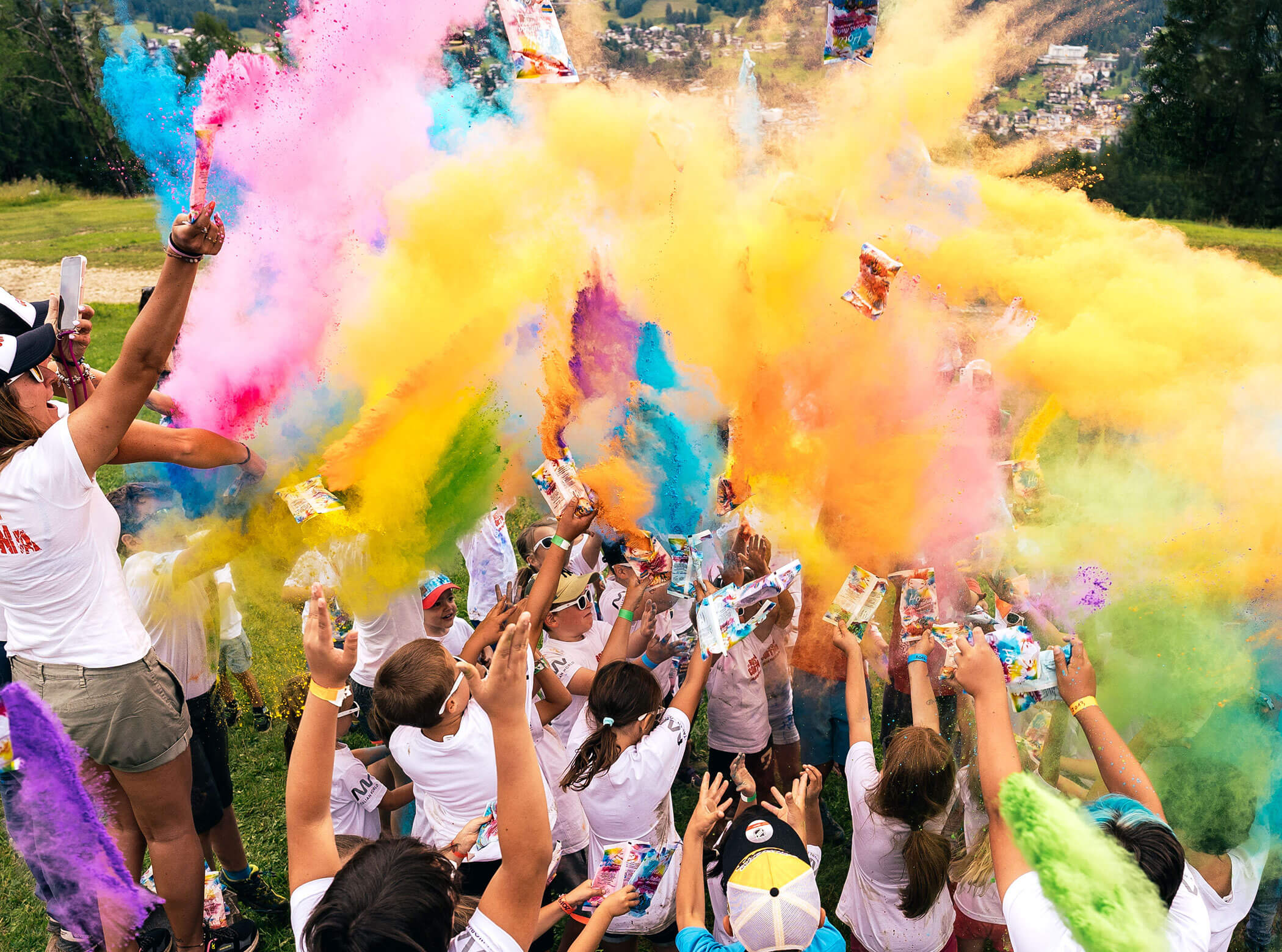 Children throw colorful powder in the air outdoors, celebrating together on a sunny day. - Scuola Sci Cortina