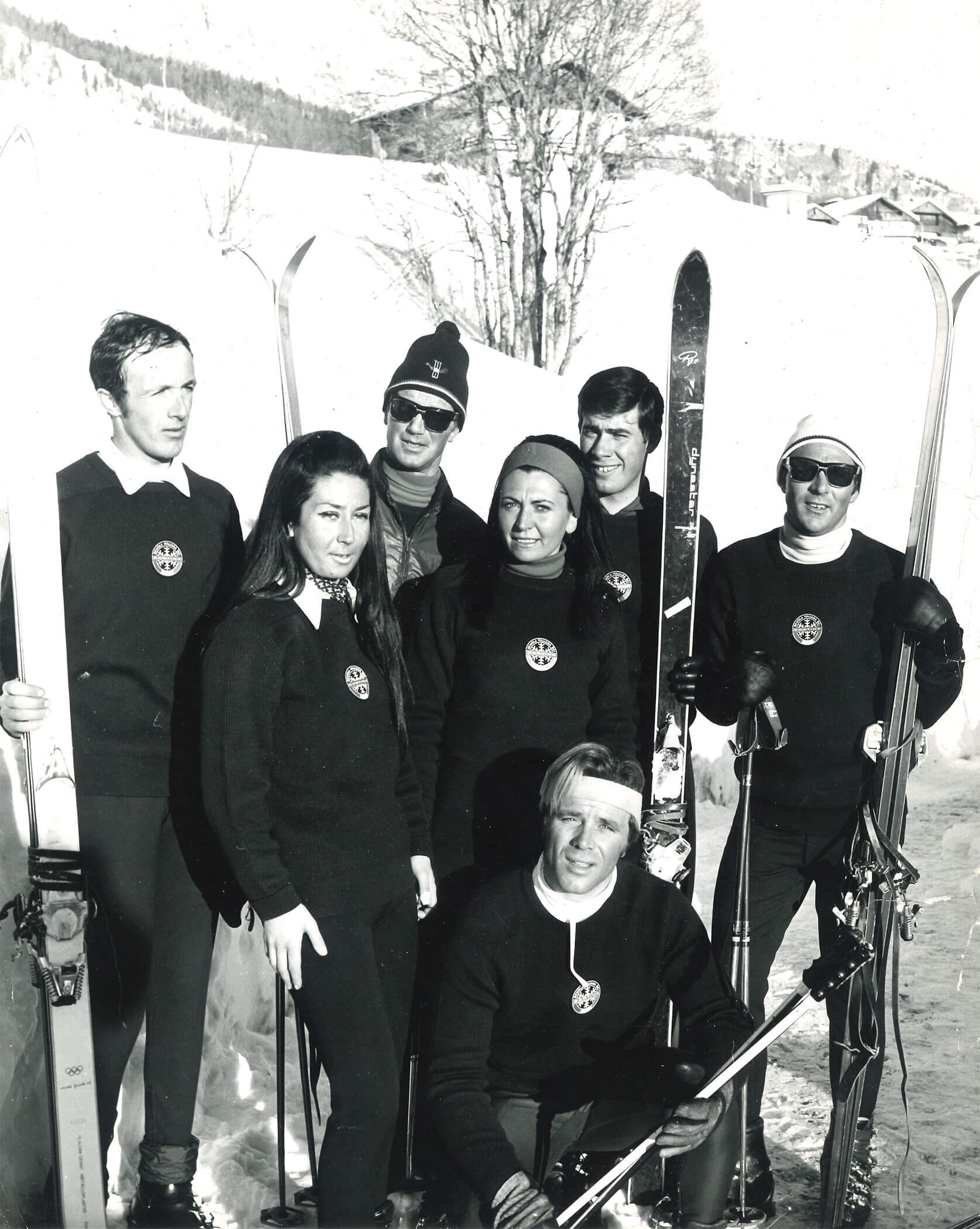 Six men and one woman in ski outfits posing outdoors in the snow with skis and poles, wearing sweaters. - Scuola Sci Cortina