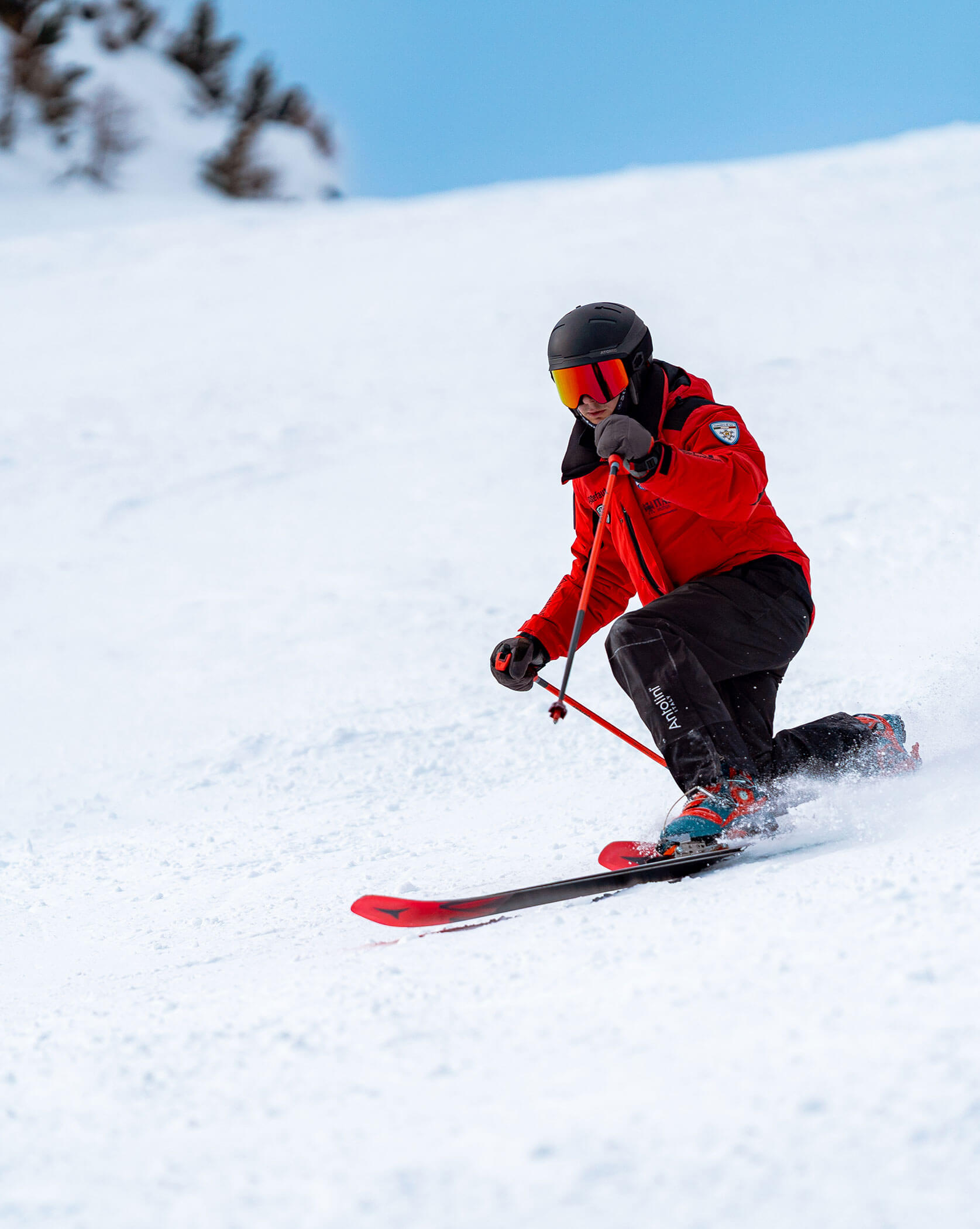 A skier in a red jacket and helmet skis downhill on a snowy slope. - Scuola Sci Cortina