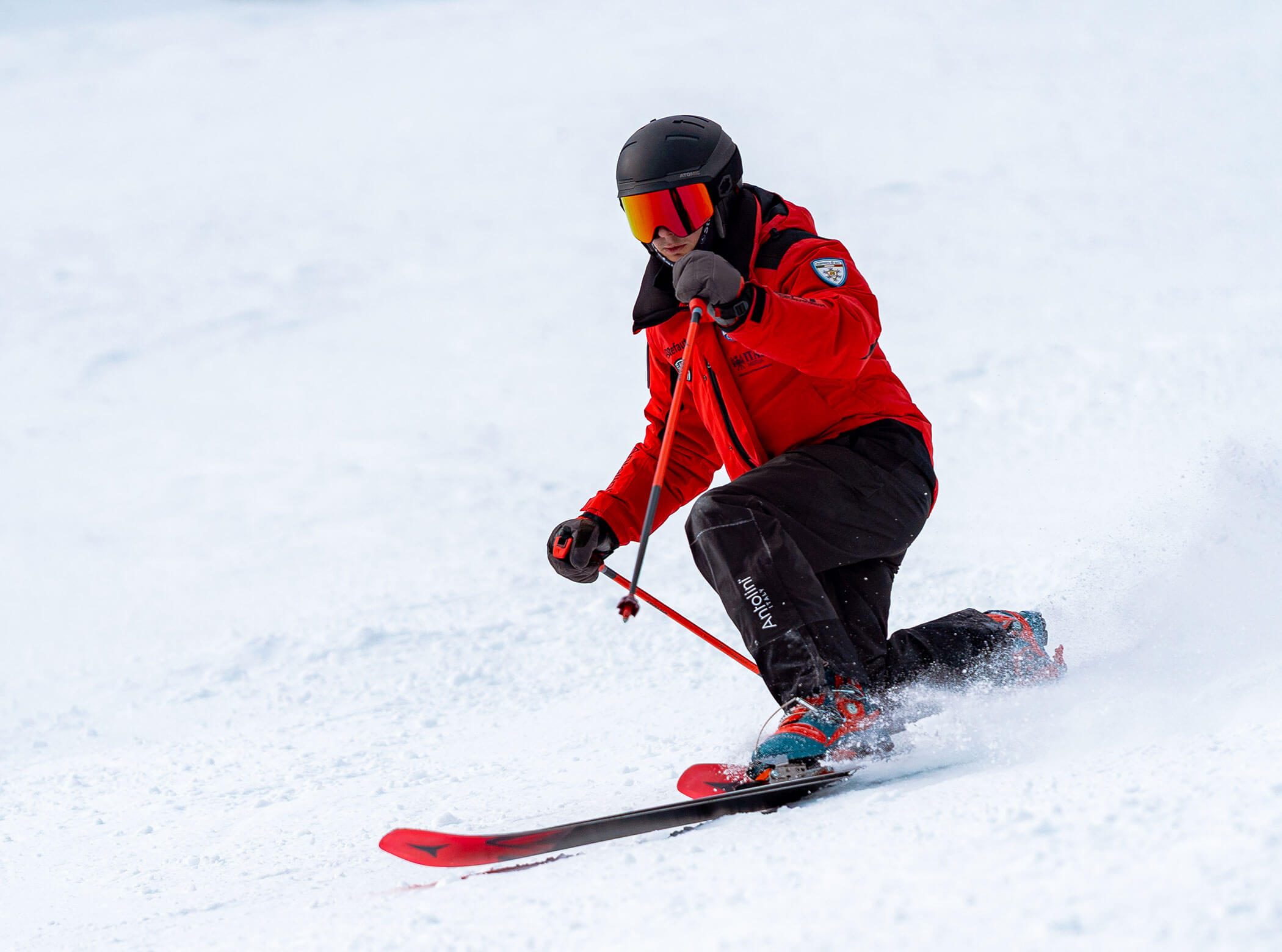 A skier in red jacket and black helmet skiing downhill on snow, holding poles and turning. - Scuola Sci Cortina