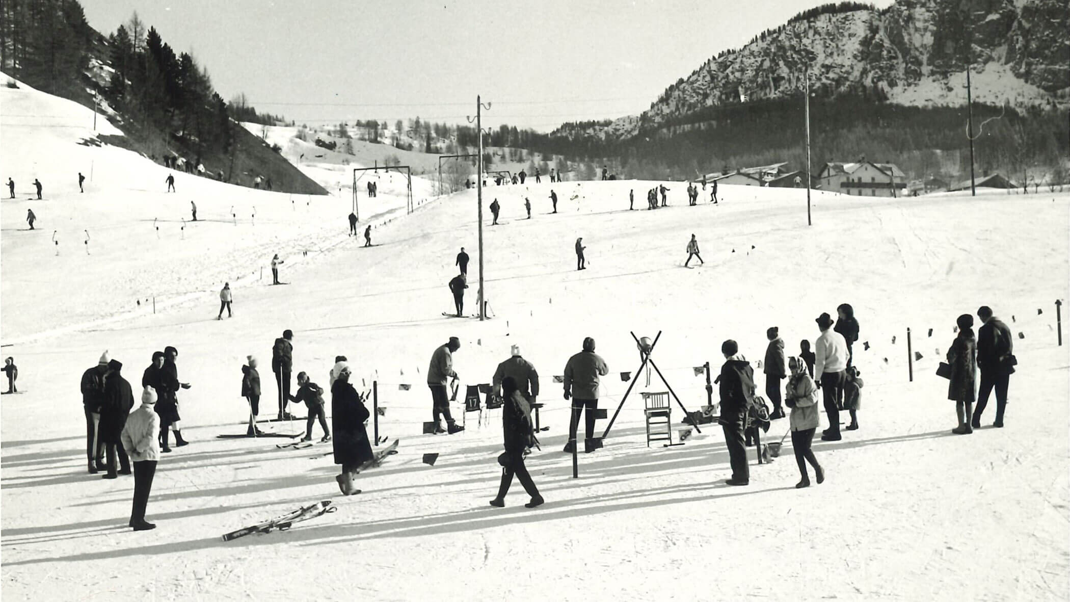 People skiing and standing on a snowy slope with mountains and trees in the background. - Scuola Sci Cortina