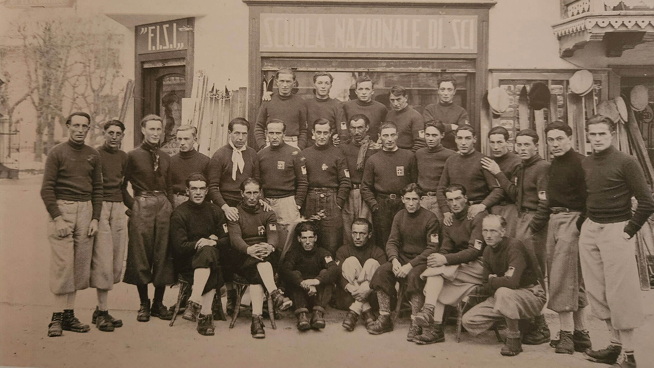 A vintage group photo of men in uniforms posing in front of a building labeled Scuola Nazionale di Sci.. - Scuola Sci Cortina